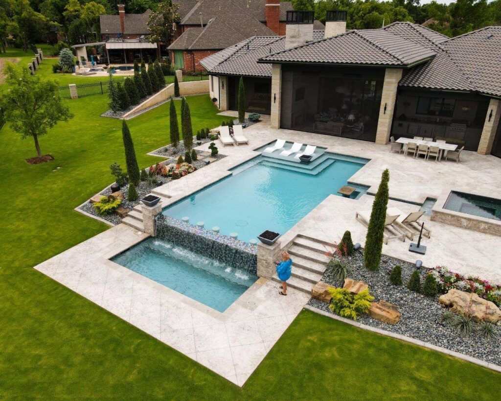 Geometric 18x38 custom pool with 7x7 interior spa and attached fire pit in Oak Tree West, Edmond OK, featuring Luna Grey coping, Shimmer Antiqua iridescent tile, and stamped concrete deck.