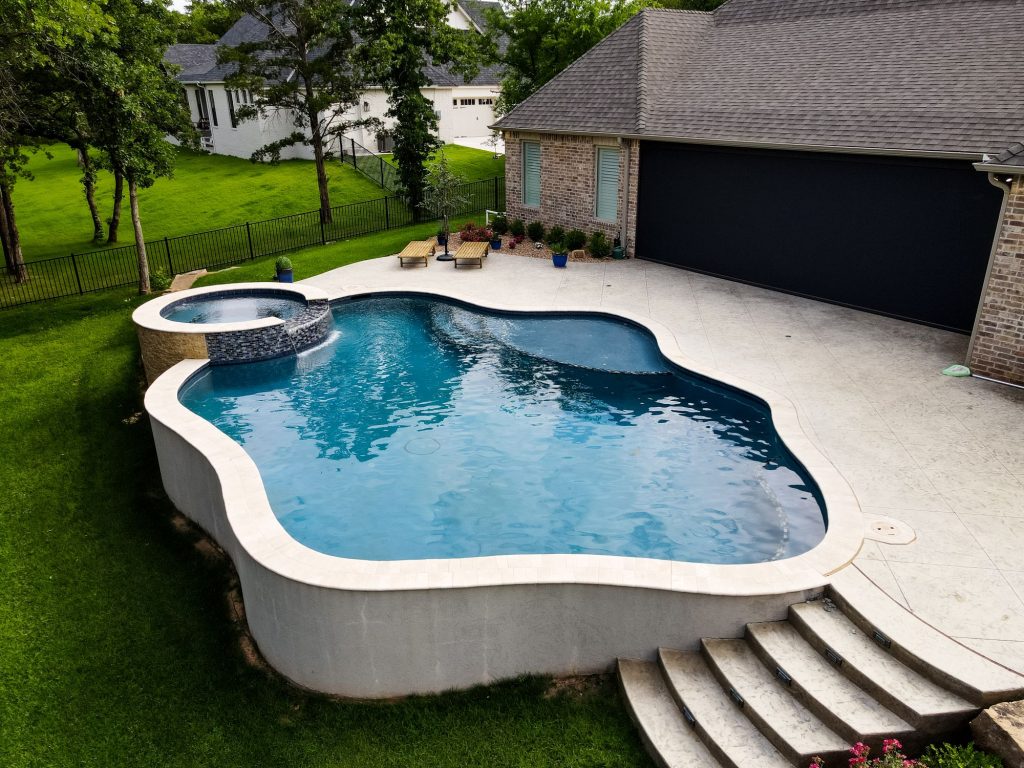 Aerial view of freeform pool with raised spa and stamped concrete deck in The Falls Jones Oklahoma.