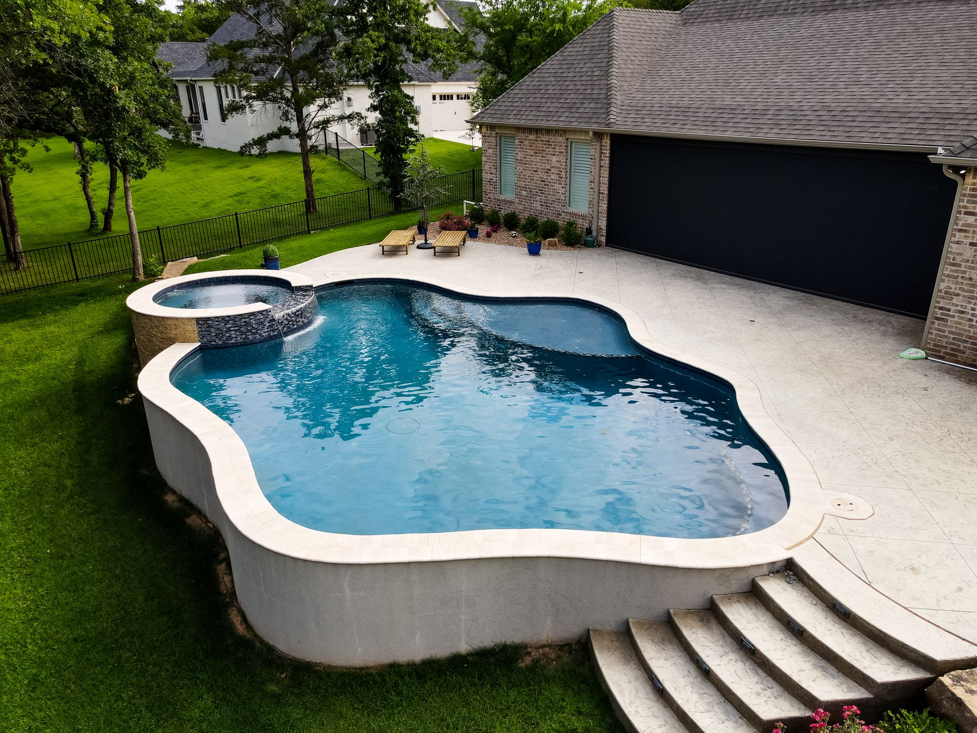 Aerial view of freeform pool with raised spa and stamped concrete deck in The Falls Jones Oklahoma.