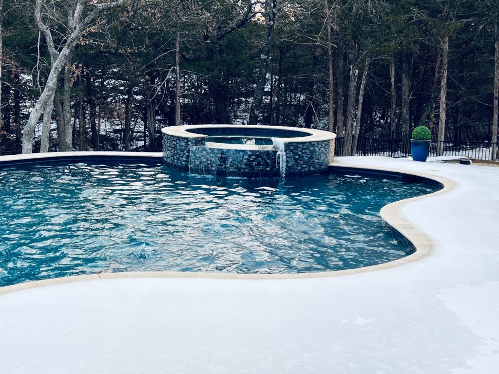 Snowy view of freeform pool with raised spa and travertine coping in Jones Oklahoma.