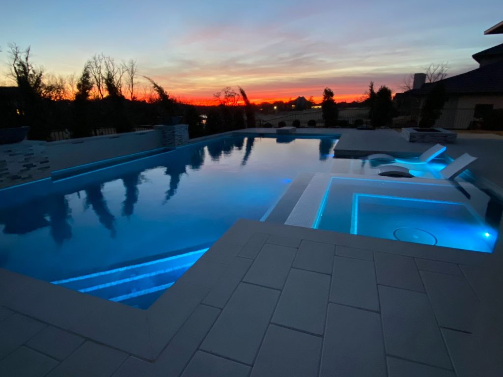 Sunset view of illuminated geometric pool and spa in Oak Tree East Edmond Oklahoma.