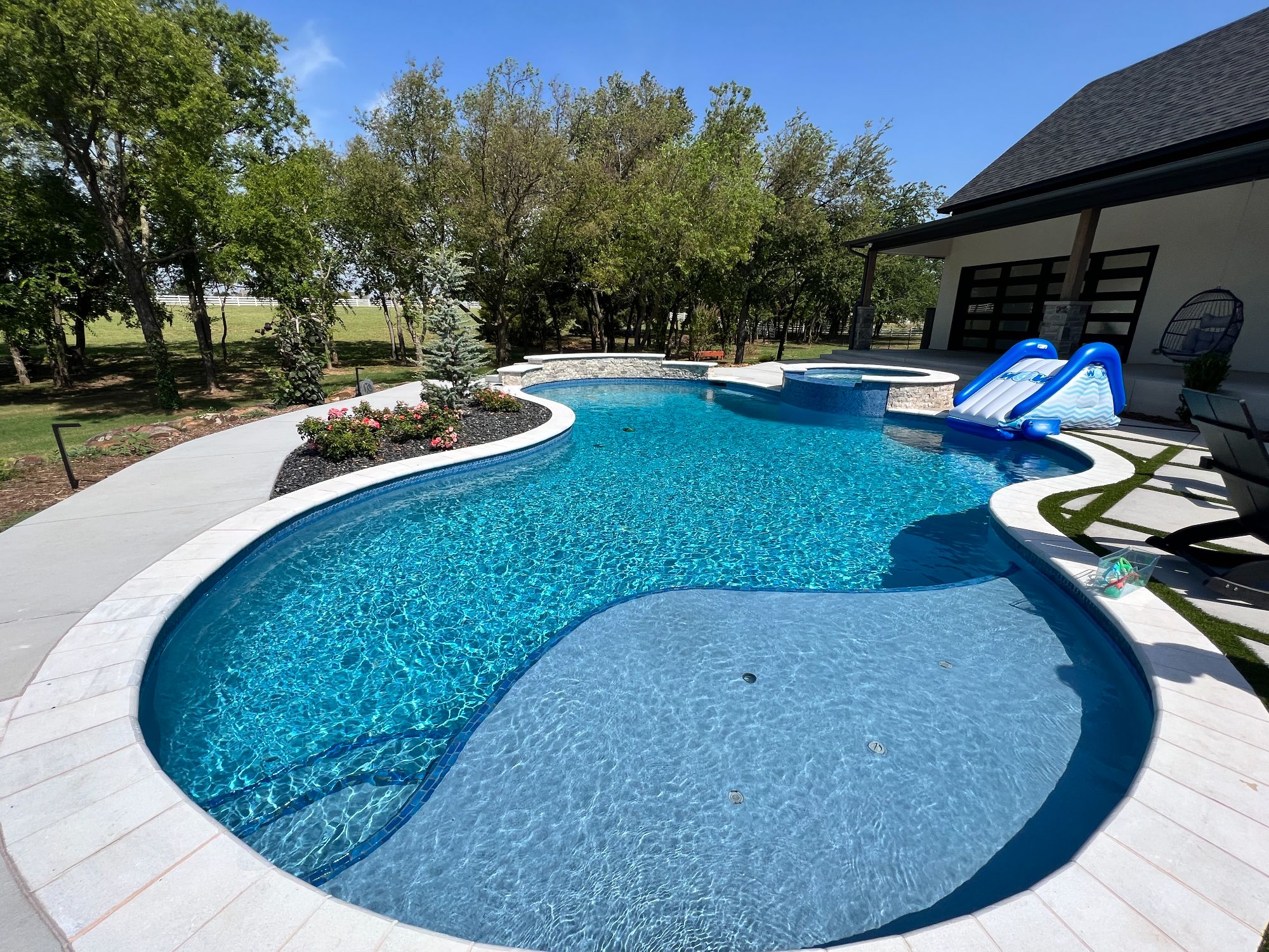 Freeform swimming pool with tanning ledge and Blue Lagoon ecoFINISH interior in Villagio Edmond Oklahoma.