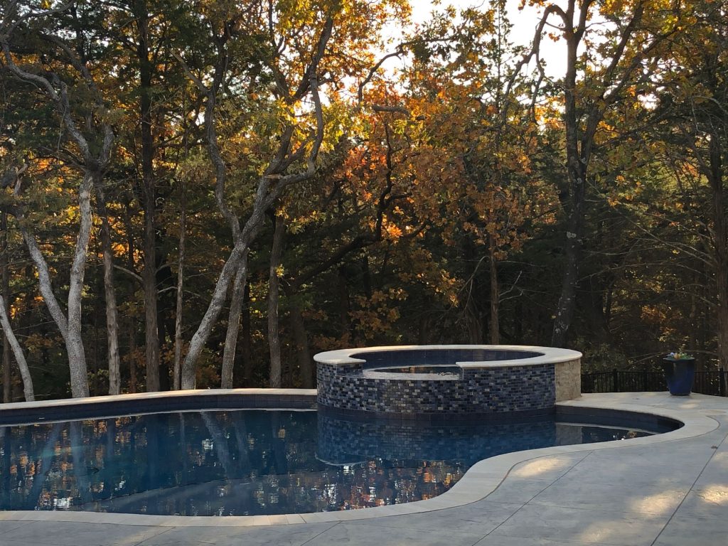 Raised spa finished with Baroque Series Blue tile and Mocha split-face stone overlooking freeform pool in Jones Oklahoma.